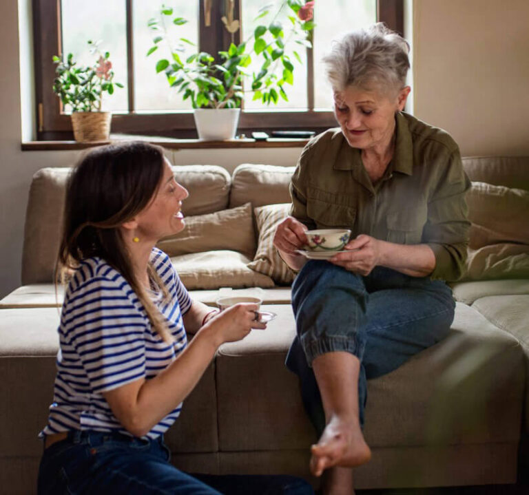 elderly mother and younger daughter talking together on couch